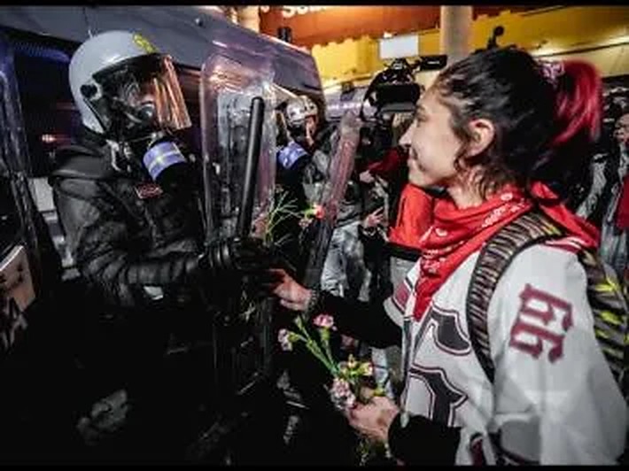 Una manifestante porge dei fiori agli agenti schierati dietro gli scudi durante il corteo del 30 ottobre